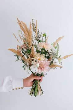 a person holding a bouquet of flowers in their hand with white and pink blooms on it