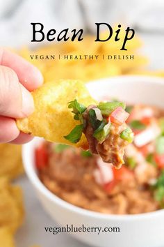 a hand holding a tortilla chip over a bowl of salsa