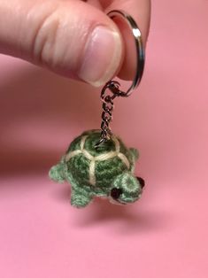 a tiny turtle keychain being held by a person's hand on a pink background