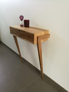 a wooden table with two vases on top of it next to a white wall