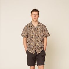 a man standing in front of a white wall wearing shorts and a shirt with a pattern on it