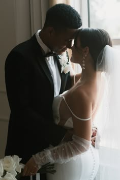 a bride and groom standing next to each other in front of a window with white flowers