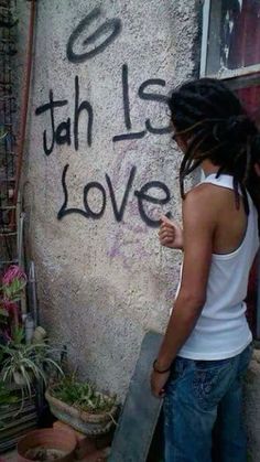 a woman with dreadlocks writing on the side of a building next to potted plants