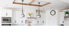 a kitchen with white cabinets and hanging lights over the stove top, along with a clock on the wall