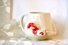 a white cup with red lips on it sitting on a table cloth next to a curtain