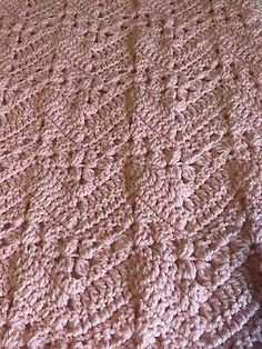 a pink crocheted blanket sitting on top of a bed