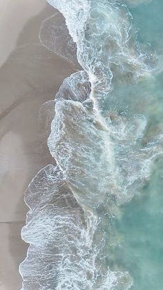 an aerial view of the ocean with waves coming in from the shore and sand on the beach