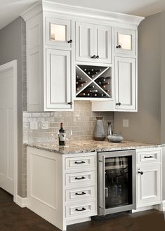 a kitchen with white cabinets and marble counter tops, wine rack in the corner on the wall