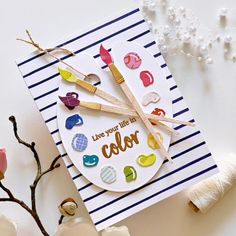 a card with paintbrushes and some yarn on the table next to it is an ornament that says, live your life in color