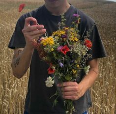 a man standing in a field holding a bouquet of wildflowers and an orange bird