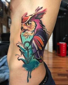 an owl tattoo on the side of a woman's leg, with colorful ink