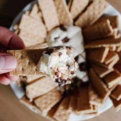 a hand holding a cracker with ice cream and chocolate chips in it on a plate