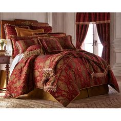 a bed with red and gold comforter set in a room next to a window