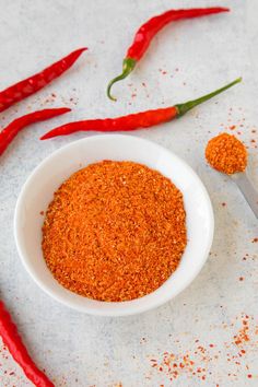 a white bowl filled with red chili seasoning next to two spoons and peppers