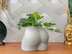 a plant in a white vase sitting on a table next to a clock and other decorative items