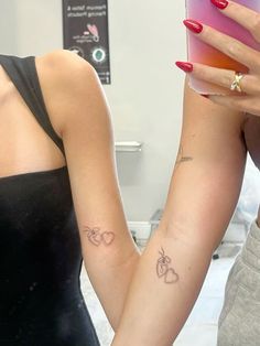 two women with matching tattoos holding each other's hands and looking at their cell phones