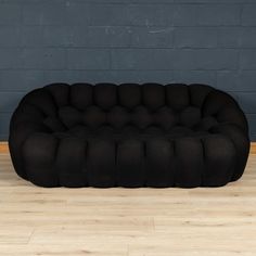 a black couch sitting on top of a hard wood floor next to a brick wall