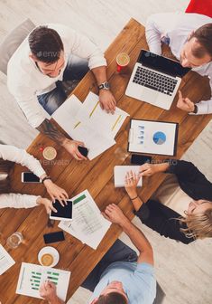 four people sitting at a table with papers and laptops