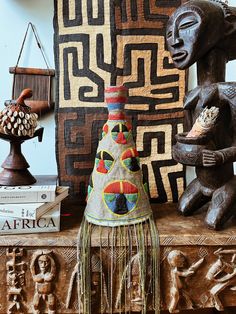 decorative items are displayed on a table in front of an african wall hanging and sculpture