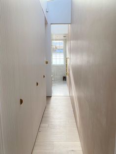 an empty hallway with white walls and wood flooring is seen in this image from the end