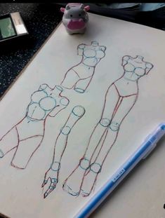 a drawing of three female mannequins on a sheet of paper next to a small toy