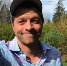 a man wearing a baseball cap is smiling at the camera with trees in the background