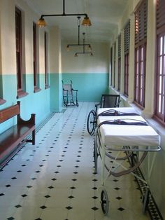 an empty hospital room with several beds and chairs on the floor, in front of two windows