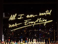 a bar with lots of liquor bottles and neon signs on the wall above it that says, all i ever wanted was everything