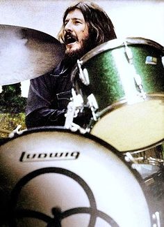 a man with long hair and beards playing drums in front of a drum set