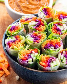 there are many colorful rolls in the bowl next to some carrots and dipping sauce