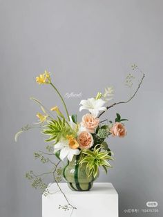 an arrangement of flowers in a green vase on a white pedestal against a gray wall