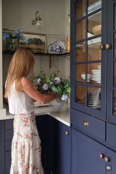 a woman standing in a kitchen next to a blue cabinet with glass doors on it