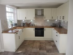 an empty kitchen with white cabinets and wood counter tops