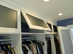 an organized closet with clothes hanging on shelves and lights above the closet doors that are open