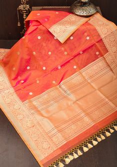 Kora is the Indian name for Pure Silk Organza, a fabric that is processed from pure natural silk. Kora silks are synonymous with regal charm and elegance. This Pink Orange Dual Tone saree has been handwoven in the timeless city of Varanasi, home of the finest silks and weaving expertise. It comes in a ravishing shade. The body of the drape features daintily woven buttons. The intricate designs of zari on the border and pallu make this saree a splendid creation. The simple motifs in gold and silv Saree Simple Look, Saree Simple, Pink Color Combination, Banaras Sarees, Kora Silk Sarees, Saree Blouses Designs, Blouses Designs, On The Border, Saree Blouses