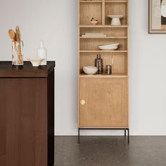 a wooden cabinet sitting next to a white wall with vases and bowls on it