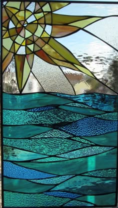 a close up of a stained glass window with blue water and sun in the background