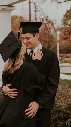 a man and woman in graduation gowns hugging each other while they are standing outside