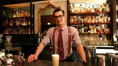 a man standing behind a bar with glasses on it