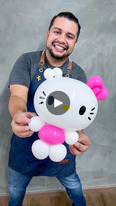 a man holding a hello kitty balloon in front of his face and smiling at the camera