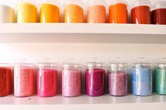 there are many different colored glitters on the shelves in this room with white shelving