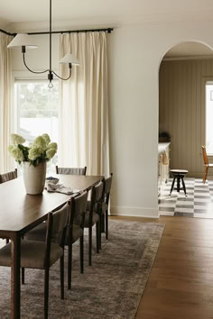 a dining room table and chairs in front of a large window with white drapes