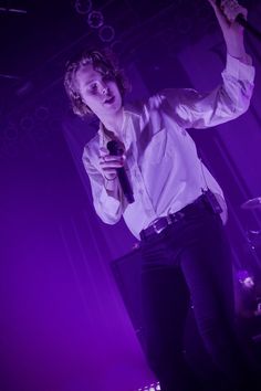 a man holding a microphone up to his mouth while standing in front of a purple light