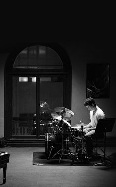 a man sitting in front of a drum set on top of a table next to a piano