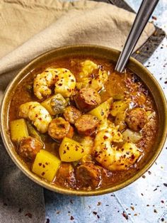 a bowl filled with stew and potatoes on top of a blue cloth next to a spoon