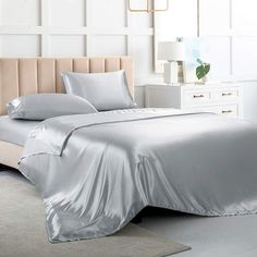 a bed with silver sheets and pillows in a white room next to a lamp on the wall