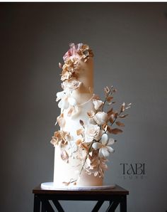 a three tiered wedding cake with flowers on the top and bottom, sitting on a table