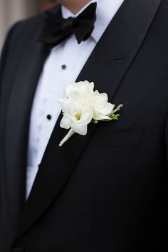 a man wearing a black tuxedo with white flowers on it's lapel