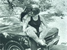 two people are sitting on the hood of a car and one person is hugging her