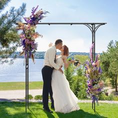 a bride and groom kiss under an arch decorated with flowers on their wedding day in front of the lake